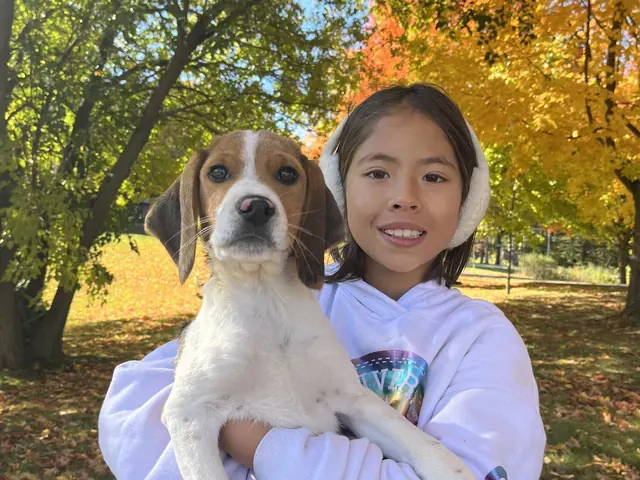 Family photo: child holding a dog beneath autumn leaves